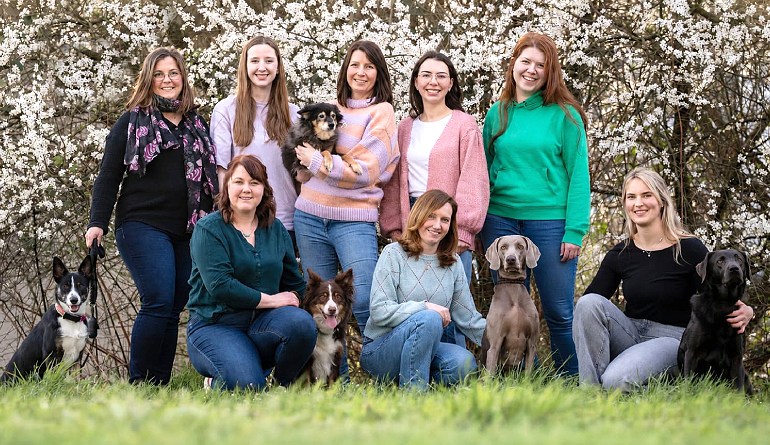 Team der Praxis westhoff steht mit Hunden beisammen vor blühenden Kirschen
